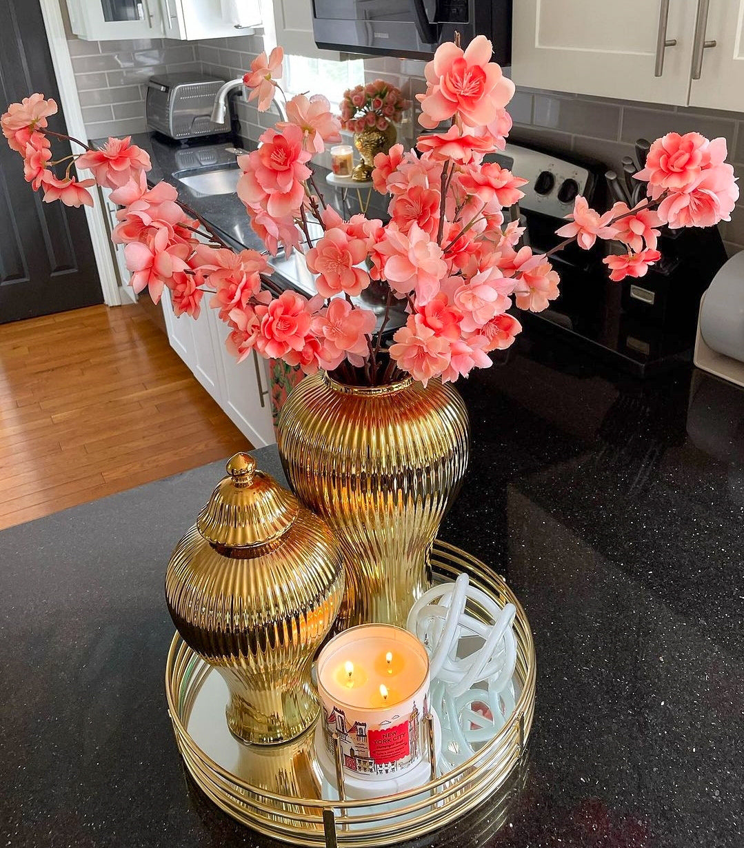 Decorative setup with pink flowers, gold vases, and a candle on a kitchen counter.