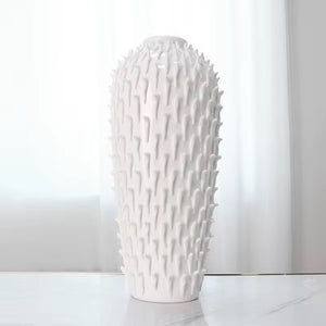 White textured vase on a white surface with a light gray curtain background