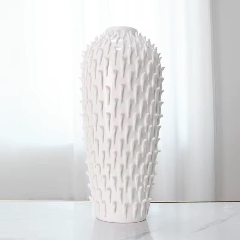 White textured vase on a white surface with a light gray curtain background